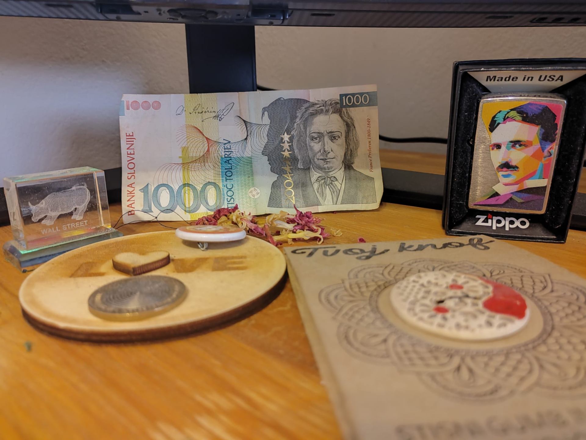 Slovenian 1000 Tolar Prešeren banknote standing on a wooden desk between a Wall Street bull glass crystal, a colorful Nikola Tesla Zippo lighter and a hand-burned wooden LOVE coin disc.